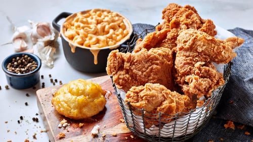 This image showcases a hearty meal of crispy fried chicken, creamy mac and cheese, and a glazed honey biscuit, set against a rustic backdrop with peppercorns and garlic. A perfect comfort food combo.
