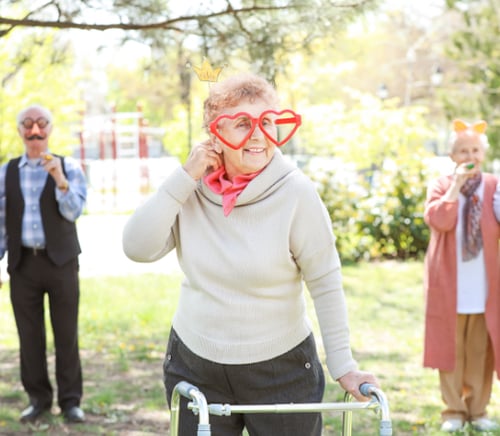 elderly woman wears gag heart glasses and walks with her walker in a park