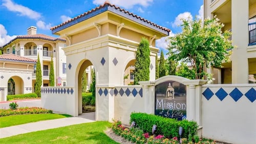Exterior entrance to apartments with green lawns, floral beds, sign, and a paved walkway at Mission at La Villita Apartments, Irving, TX, 75039