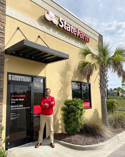Agent Charlie Nash standing and smiling wearing red State Farm shirt and tan khaki pants outside of agency