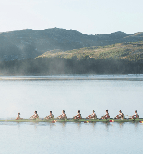 A rowing team going across a calm lake with mountains in the background.