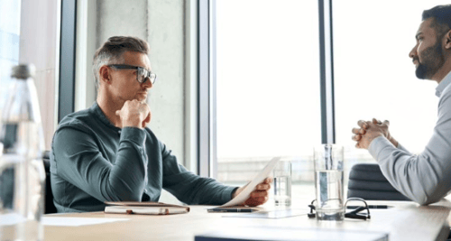Young doctor reviewing a retirement and tax strategy with his financial planner at an office desk, discussing IPP vs. RRSP options.