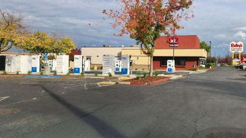 Several EVgo fast-charging units installed in marked parking spaces at a public charging station, with EVgo logos on the chargers, protective bollards around each unit