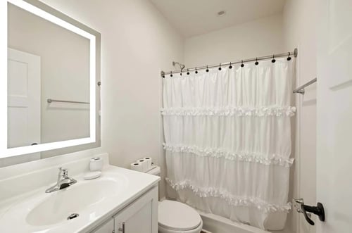 Modern Belle Meadow apartment bathroom with a white vanity, a large lighted mirror, and a tub/shower unit with a sleek curved rod.