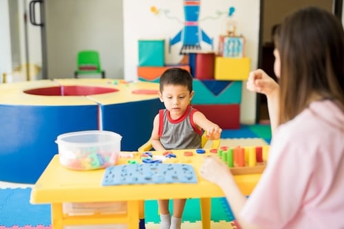 Therapist and child smiling during a playful ABA session in a colorful therapy room, representing one-on-one tailored autism services.