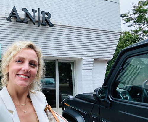 Ashley-Nicole standing and smiling in fornt of white and grey building with black AN|R sign