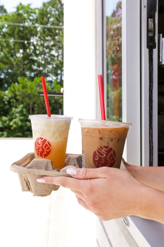 Hand passing a drink carrier with three iced Sweetwaters beverages through a drive-thru window.