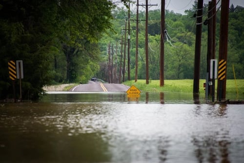 Road closed sign sitting in deep floodwaters on a rural road.