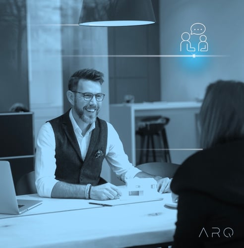 Ein lächelnder Mann mit Brille und Bart (Thomas Döring) sitzt an einem hellen Bürotisch gegenüber einer Person, deren Rücken zur Kamera zeigt. Der Raum scheint modern und hell mit großen Fenstern im Hintergrund zu sein. Ein stilisiertes Symbol für eine Unterhaltung ist in der oberen linken Ecke überlagert, und das Logo 'ARQ' ist unten rechts sichtbar."