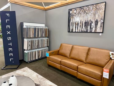 Genuine leather Flexsteel sofa in warm tan with fabric sample wall at Slumberland Furniture Burlington. Customize your Flexsteel furniture locally in Burlington, Iowa.