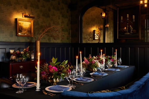 Candlelit dining table with floral centerpieces in a dark-paneled room.