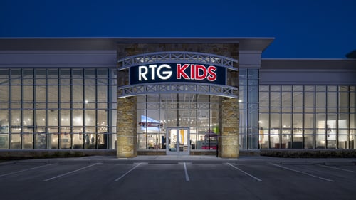 Nighttime exterior of RTG Kids at Rooms To Go in Pearland, TX, showcasing illuminated signage and large glass windows.