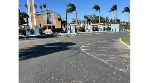 EVgo fast charging stalls in a row beside a church, with white chargers, blue bollards and a gray power cabinet