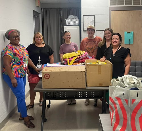 Agent Kasey and five team members inside a room with a table filled with boxes and a target bag