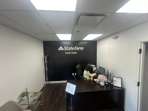 White and black walls with silver State Farn sign. Brown desk with computers in office