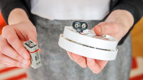 An individual installing a 9V battery into a smoke detector to ensure home safety.