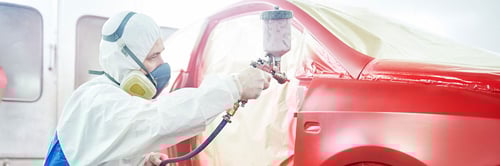 A person in protective gear spray painting a car red.