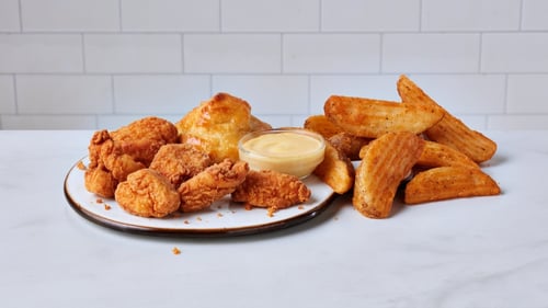 This image features crispy Cajun-seasoned chicken nuggets in a colorful box, with a creamy dipping sauce on the side. A perfect combination of flavorful and mild seasoning for a tasty snack.