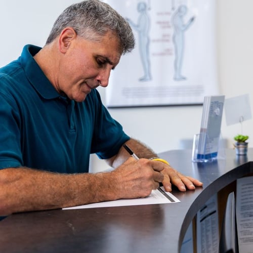 Man filling out new patient forms at the front desk of CT Junction Brain & Spine.