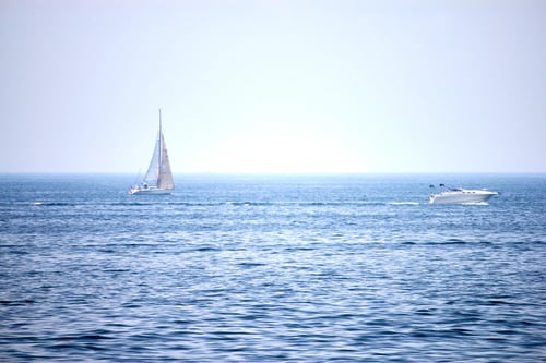 Serene ocean scene with a sailboat and speedboat.
