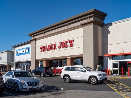 Cars passing on road in front of Trader Joe's and Five Below stores.