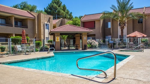 A swimming pool surrounded by a fence and umbrellas in front of a building at West 35th Apartments, Arizona, 85053
