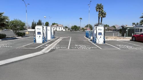 Several EVgo fast-charging units installed in marked parking spaces at a public charging station, with EVgo logos on the chargers, protective bollards around each unit