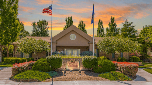 A house with a flag on top of it is surrounded by trees and bushes at Prairie Commons - 55+ Senior Community Apartments, Kansas, 66049