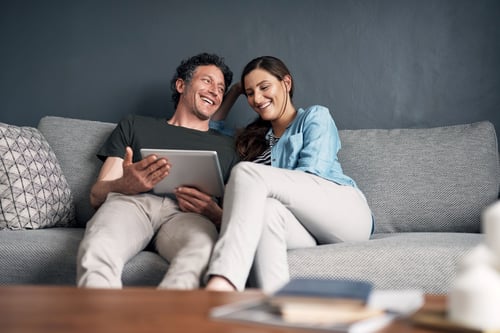 Man and woman with laptop laughing while sitting on couch