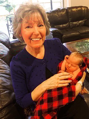 Smiling woman holding newborn baby while sitting on a couch