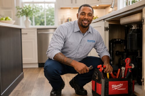 bluefrog plumber kneeling in a kitchen with professional plumbing tools ready for service