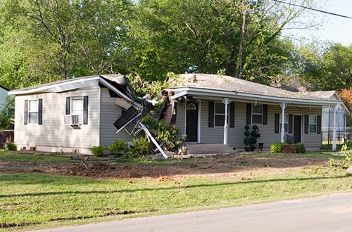 A home damaged by a fallen tree after a recent storm. The roof, porch, and a large portion of the home sustained significant storm damage.