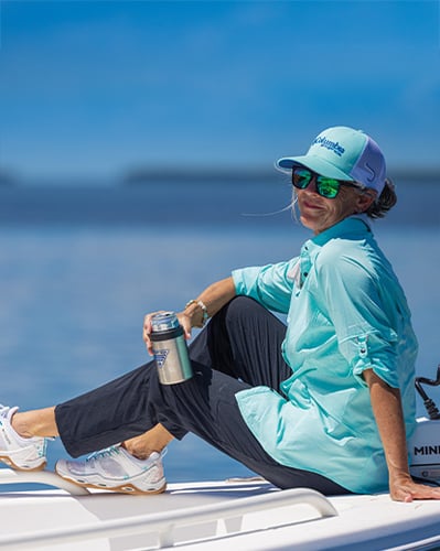 Woman sitting on boat with sun protection clothing and drink in hand