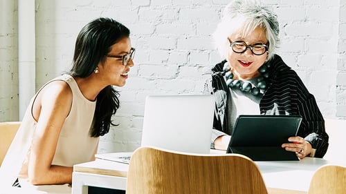Two women looking at computer screens and smiling.