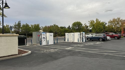 Several EVgo fast charging units installed in marked parking spaces at a public charging station, with EVgo logos on the chargers, protective bollards around each unit