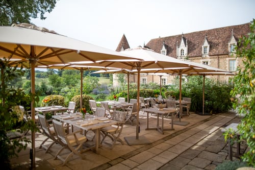 Alfresco dining with château views and lush gardens under shaded parasols.
