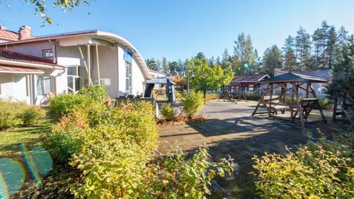 Kuvassa on toimipisteen piha, joka on laatoitettu ja sitä reunustaa pensaat. Pihassa on puinen pihakeinu.
