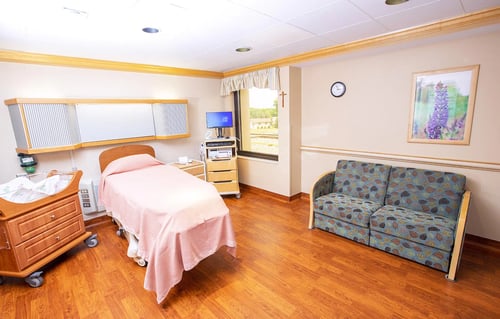 A view of the labor and delivery room showing bassinet, birthing bed, sofa and birth monitoring equipment.