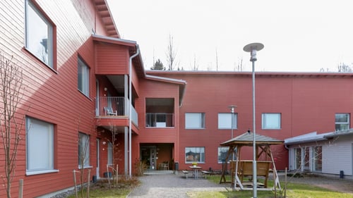 Tuulikanteleen punainen kaksikerroksinen rakennus. Etualalla keinu.