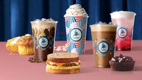 A variety of holiday Caribou Coffee beverages surrounded by a Pumpkin Cream Cheese Muffin, French Toast Sandwich, and Chocolate Truffle Brownie, creating a cozy and indulgent atmosphere.