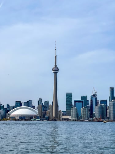 Toronto skyline, featuring the CN Tower among modern skyscrapers. The foreground shows calm water, creating a serene urban scene.