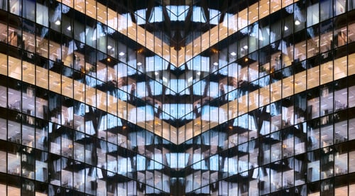 close up of sky scraper at night with illuminated windows and reflection of neighboring buildings