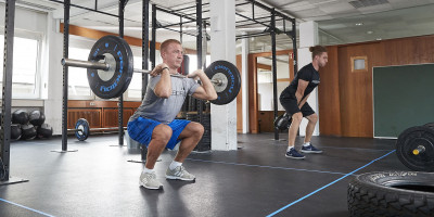 Zwei Männer trainieren im Fitnessstudio von AFS Athlethik in Stuttgart mit Langhanteln, einer macht Kniebeugen, der andere hebt Gewichte.