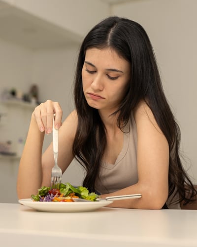 Woman at a table looking reluctantly at a plate of food.