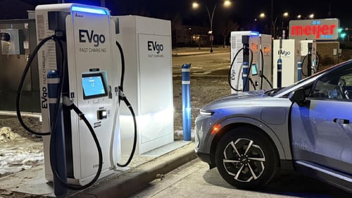 Several EVgo fast-charging units installed in marked parking spaces at a public charging station, with EVgo logos on the chargers, protective bollards around each unit