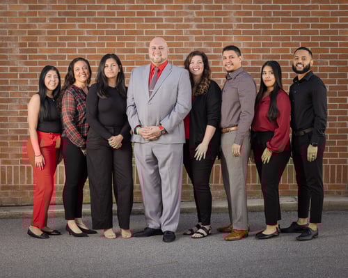 Agent Ramey standing and smiling with seven team members wearing professional attire