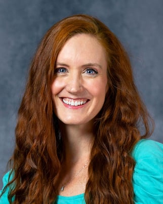 Kaia is smiling in front of a gray backdrop with a light blue top.