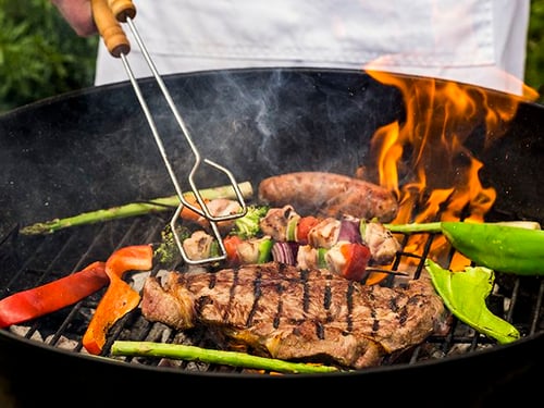 Person grilling steak and vegetables on a grill
