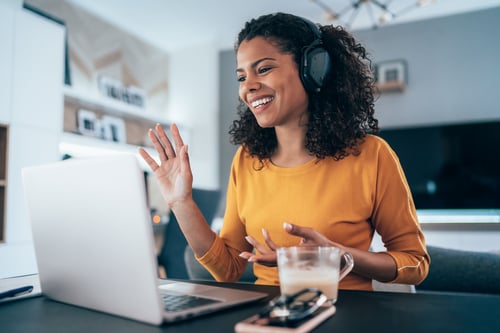 Woman sitting at a desk in front of a laptop waving.
