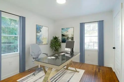Light-filled home office with a sleek desk, modern chair, abstract artwork, and windows on two walls.